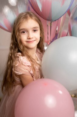 Helyumla şişirilmiş balonların arka planında pembe elbiseli güzel bir kız. Mutlu çocuk.