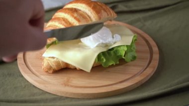 Beyaz tabakta haşlanmış yumurta ve kruvasan ile tost. Aşçı haşlanmış bir yumurtayı bıçakla keser. Yumurta sarısı çıkıyor..