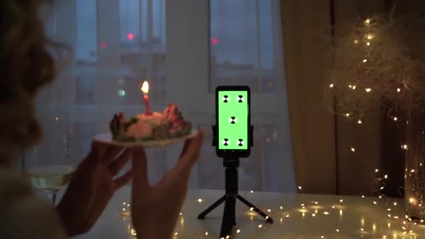 Schermo verde e tasto cromatico dello smartphone. una donna tiene un pezzo di torta con una candela accesa e spegne la fiamma. concetto di compleanno online. — Video Stock