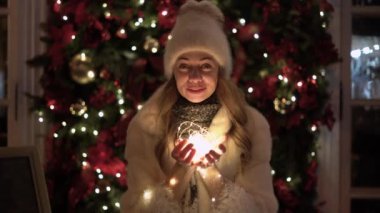 Kış tatilini kutlamak için kıvılcımlar kullanarak sıcak kahve içen sıcak giysili genç bir bayan. Gece şehir sokağında çelenk ışığıyla eğlenen genç bir kadın..