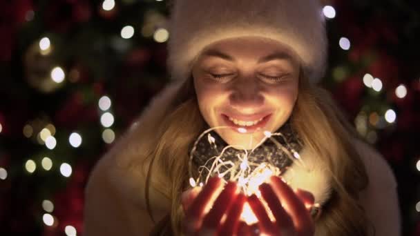 若い美しい女性の肖像画です。帽子の中の冬の屋外の女性は彼女の手の中にガーランドを保持し、願いを作ります。コンセプトお祝いクリスマス新年. — ストック動画