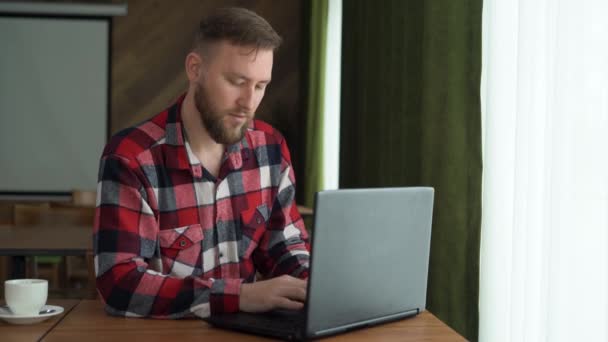 Maschio caucasico utilizzando il computer portatile, seduto a tavola in ufficio, digitando sulla tastiera e guardando lo schermo, godendo di lavoro a distanza, messa a fuoco selettiva. — Video Stock