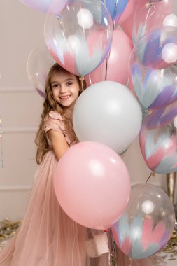 Helyumla şişirilmiş balonların arka planında pembe elbiseli güzel bir kız. Mutlu çocuk.