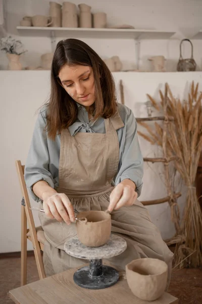 一位年轻的女工匠在创意工作室里做陶器的同时 专心致志地雕琢一只生粘土碗 一位女陶瓷店主在一家手工制作的陶器零售店里做手工艺品出售 复制空间 — 图库照片