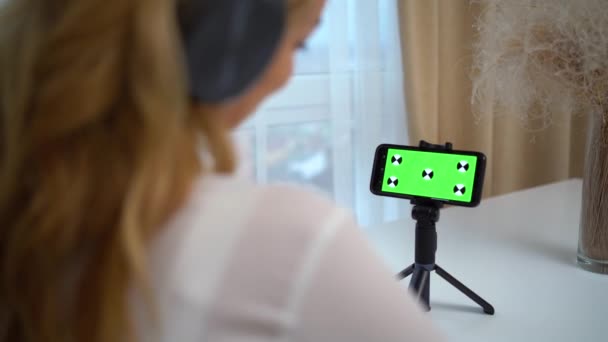 Egy kaukázusi nő háta mögötti kép egy videóhívás során. Fiatal nő használja okostelefon zöld képernyős mockup az online hívás. — Stock videók
