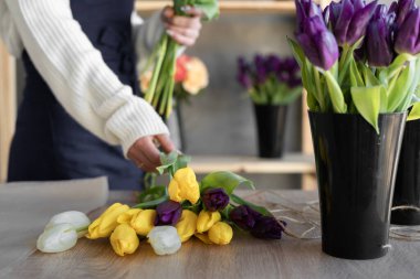 Çiçekçi kadın bir buket sarı lale yapıyor. Atölyedeki ustanın ellerine yakın plan bir buket al. Boşluğu kopyala.