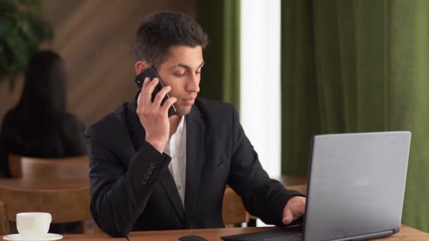 Empresário árabe sério falando ao telefone, usando um laptop, tendo uma conversa de negócios, gerente de RH realizando uma entrevista em um telefone celular, aconselhando os funcionários, fazendo uma oferta de venda — Vídeo de Stock