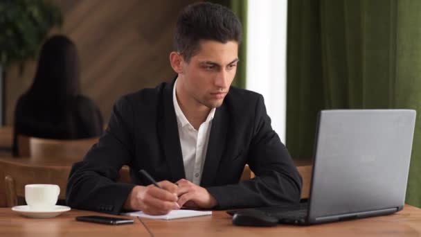 İş planlaması, e-öğrenme, online öğrenme konsepti. Arap erkek iş adamı deftere yazar ve ofisteki bir dizüstü bilgisayarda çalışır. Erkek öğrenci dizüstü bilgisayarla, not defteriyle çevrimiçi kurs okuyor. — Stok video