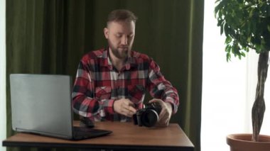 Profesyonel erkek fotoğrafçı kameranın kapağını açar, bir flaş bellek çıkarır ve bir laptopa veri yüklemeye başlar..