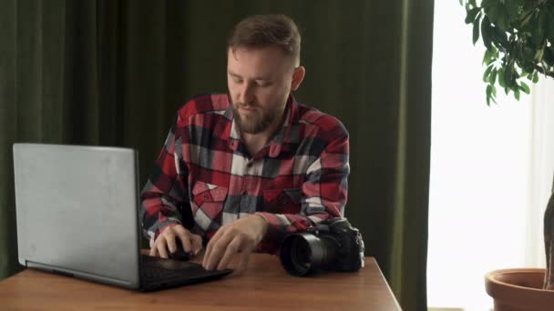 Müder männlicher Fotograf mit Kopfschmerzen am Arbeitsplatz zu Hause am Laptop. — Stockvideo