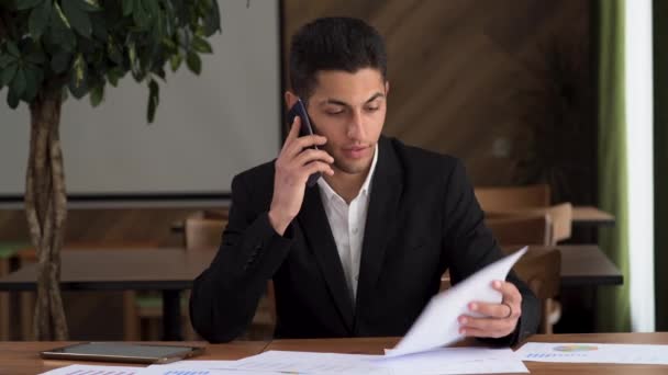 Ένας χαμογελαστός Άραβας επιχειρηματίας τηλεφωνεί στο χώρο εργασίας. Ευτυχισμένος επιχειρηματίας που μιλάει στο κινητό σε ένα απομακρυσμένο γραφείο. Πορτρέτο ενός κορυφαίου διαχειριστή ανάγνωση εγγράφων με καλά αποτελέσματα — Αρχείο Βίντεο