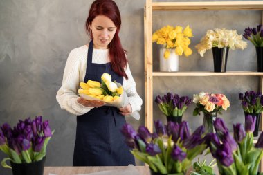 Çiçekçinin gülümseyen portresi çiçeklerle çevrili bir vitrinin yanında önlüğün içinde duruyor. Boşluğu kopyala.