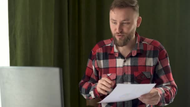 Joven hombre de negocios caucásico durante la videollamada habla y señala la mano en la carta gráfica de información. Presentación en línea de un plan de negocio para alcanzar objetivos. — Vídeos de Stock