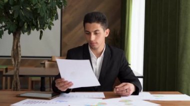 Konsantre olmuş genç Arap işadamı pazarlama araştırma raporuna bakıyor, grafiklerdeki istatistiksel verileri analiz ediyor, büyüme stratejisi geliştiriyor, modern ofiste tek başına çalışıyor.