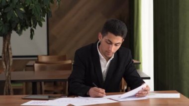 Konsantre olmuş genç Arap işadamı pazarlama araştırma raporuna bakıyor, grafiklerdeki istatistiksel verileri analiz ediyor, büyüme stratejisi geliştiriyor, yalnız çalışıyor.