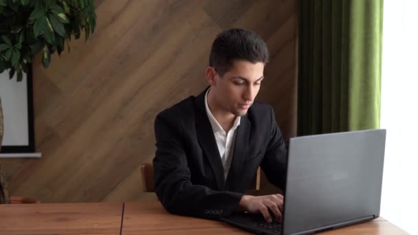 Jovem árabe masculino usando computador portátil, sentado à mesa no escritório em casa, digitando no teclado e olhando para a tela, desfrutando de trabalho remoto — Vídeo de Stock