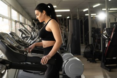 Kardiyo çalışması. Spor giyim kuşamında spor salonunda spor ya da spor kulübünde egzersiz yaparken hız ayarlayan mutlu bir atletik kadın. Boşluğu kopyala.