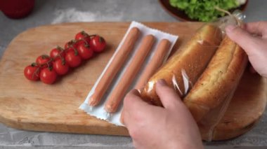 Erkek eli, sosisli sandviç yapmak için paketten iki çörek alır..