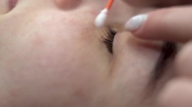 Genç bir kadın kirpik uzatma prosedüründen geçer ve maskarayı pamuklu bezle temizler ve güzellik salonuna yapışır. Göz kapağı hazırlığı.