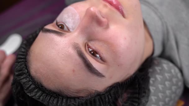 Eyelash extension stylist increases eyelashes for a client. Beautician in a beauty salon puts a patch on eyes of a girl client. — Stock Video