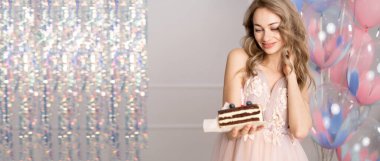 Milenyum kadını bir bayram ya da kutlama düzenliyor. Pembe elbiseli güzel bir kadın elinde helyum balonlarında mumlarla bir parça kek tutuyor. Pankart. Boşluğu kopyala.
