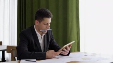 Düşünceli bir Arap adam, masadaki modern iç mekanda otururken dijital tablet ekranına bakıyor. İş adamı, ofiste metin ya da e-kitap okuyor.