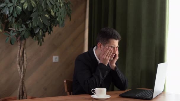 Upset arabic young man massages the bridge of his nose, feels tired eyes after a long work with a laptop, business guy sits in a cafe, tired man feels discomfort and eye pain, poor vision — Stock Video