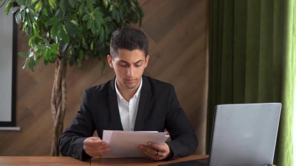 Retrato de um analista de negócios árabe a trabalhar num portátil. Vista de câmera de um local de trabalho de escritório com um computador e documentos financeiros. Design de ocupação de negócios com um jovem — Vídeo de Stock