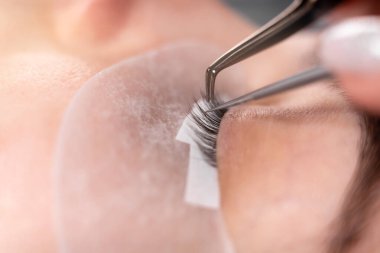 Kirpik uzatma prosedürü. Ustanın aletine yakın çekim. Cımbızlar seyrek kirpikleri yayar, uzatmaya hazırlanırlar.