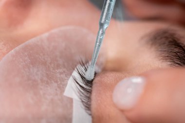 Spa salonunda kirpik uzatma prosedürü. Yakından bakınca, usta kirpikleri bir çözeltiyle temizliyor..