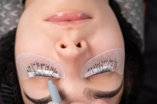 Eyelash extension procedure. The master with tweezers forges long eyelashes to beautiful female eyes. the master makes a marking with a marker.