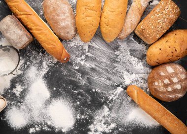 Un, taze sıcak hamur işleri, buğday unu, ekmek üretimi konsepti ve yazı yazılacak yer içeren siyah bir zemin üzerine serilmiş geniş bir ekmek çeşitliliği.