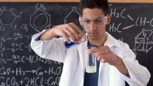 Estudiante árabe joven en una lección de química muestra una reacción química al mezclar dos sustancias líquidas durante un laboratorio contra el fondo — Vídeo de stock