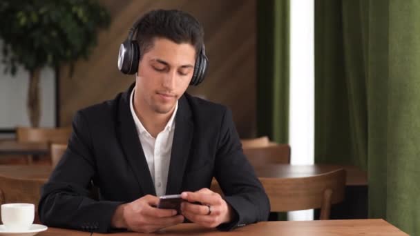 Young arab man connecting headphones to smartphone listening to music, listening to songs from phone in cafe, music tracks — 비디오
