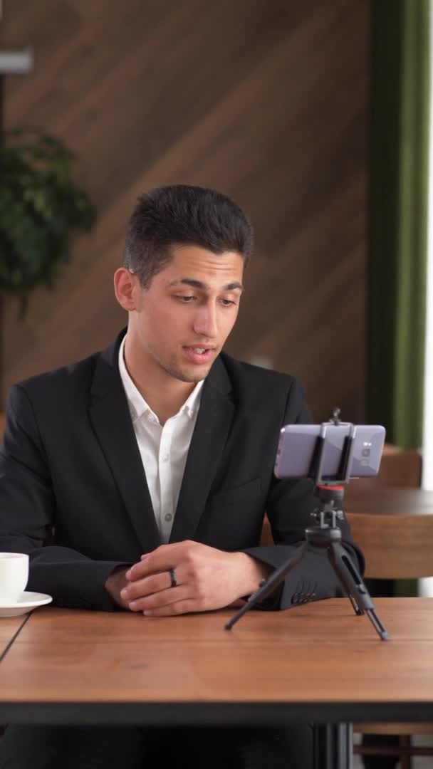 Arabic blogger recording video in cafe, young 20s male holding online webinar using smart phone, businessman working on video call in coffee shop, vertical — Vídeos de Stock