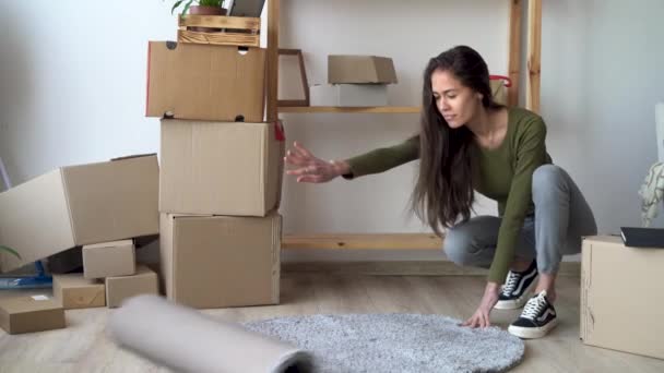 Nuovo concetto di casa, una giovane donna che stende un tappeto in una stanza gode del processo di creazione di intimità, mettendo le cose in ordine nel soggiorno. Spostamento — Video Stock