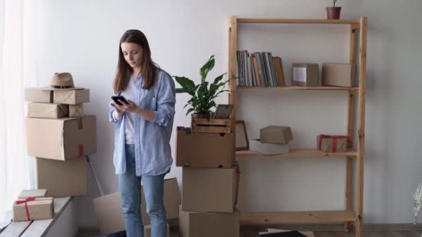 Vrouw die naar een nieuw huis verhuist, aan de telefoon praat met een vervoerder die dingen naar huis brengt, zich in een appartement vestigt en dingen in dozen, verhuizing — Stockvideo