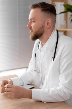 Ofiste masada çalışan bir erkek doktorun yan görüntüsü. Ciddi doktor hastayı bekliyor. Parlak bir ofisteki bir doktorun portresi çalışmaya hazır. Boşluğu kopyala.