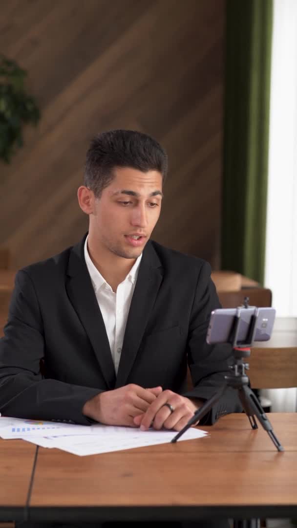 Young business Arab, an influential man sitting in the office records a video blog on a smartphone. 20s biracial manager talking filming live video on mobile phone with colleagues — Vídeos de Stock