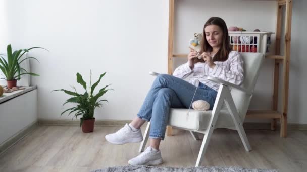 Kaukasische junge Mädchen stricken auf einem Stuhl zu Hause sitzen, das Konzept des Strickens und Handarbeiten, Frauen Hobbys und Freizeit, Stricken — Stockvideo