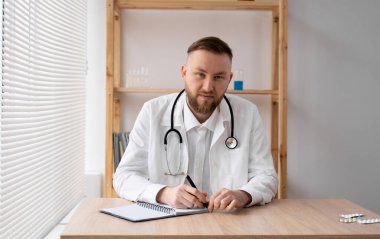 Mutlu genç doktor beyaz tıbbi ceket giyer ve steteskop kameraya bakar. Gülümseyen doktor, pratisyen hekimler bir hastaya video üzerinden danışmanlık yapıyor. Yakın plan vesikalık portre. kopyala