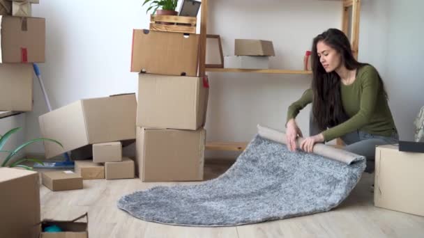 Yeni bir ev kavramına taşınan genç Latin kadın, taşınma ve yer değiştirme, yenileme süreci için halı ve kutu topluyor — Stok video