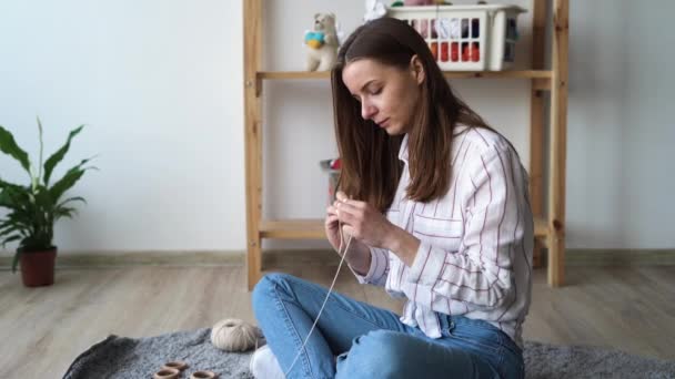 Hobby- och handarbetskoncept, stickning av ung kvinna stickning av virkhalsduk med ulltrådar sittande på golvet, fritid — Stockvideo