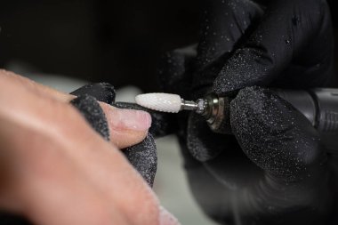 Manikürcü, kadın parmaklarındaki maniküre elektrikli tırnak matkabı uyguluyor. Bir kadın manikür yaptırıyor. Güzellik uzmanı müşterinin tırnaklarındaki eski jöle cilasını çıkarıyor. yakın plan