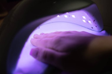 UV lambada manikürlü kadın eli. Jel cilası kurutmak için. Güzellik salonu konseptinde manikür.