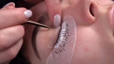 Güzellik salonundaki kirpik uzantıları, cımbızla kirpiklerini düzelten güzellik hocası, gözlerindeki yapay saç uzantıları.