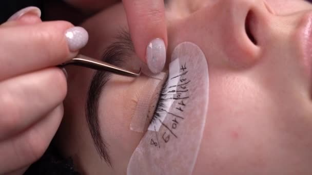 Eyelash extensions in a beauty salon, beauty master straightening eyelashes to a woman with tweezers, the process of artificial hair extensions on the eyes — Vídeo de Stock