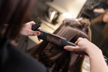 Kaplıca salonundaki ustanın ellerini yakın plan yap. Saçını kaplıca salonundaki ütüyle düzelt. keratin saç restorasyonu ve protein saçı