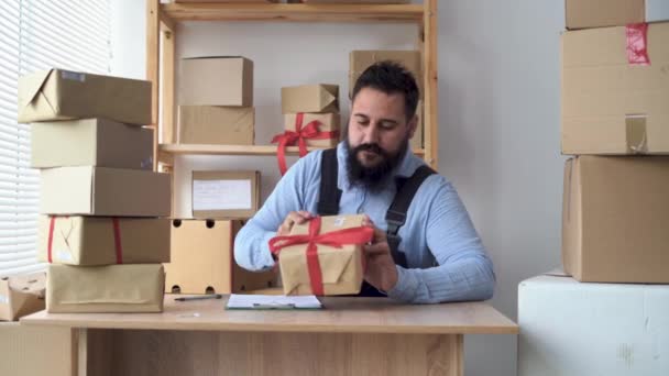 Bebaarde hindoe mannelijke ondernemer werken vanuit huis in uniform met verpakking doos op de werkplek - online kopen of verkopen online concept. — Stockvideo