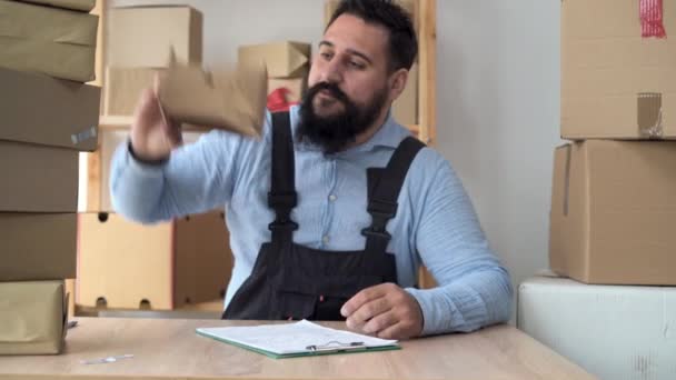 Bearded hindu male business owner working from home in uniform with packing box at workplace - online buying or selling online concept. Counts boxes of goods and keeps records. — Vídeo de Stock